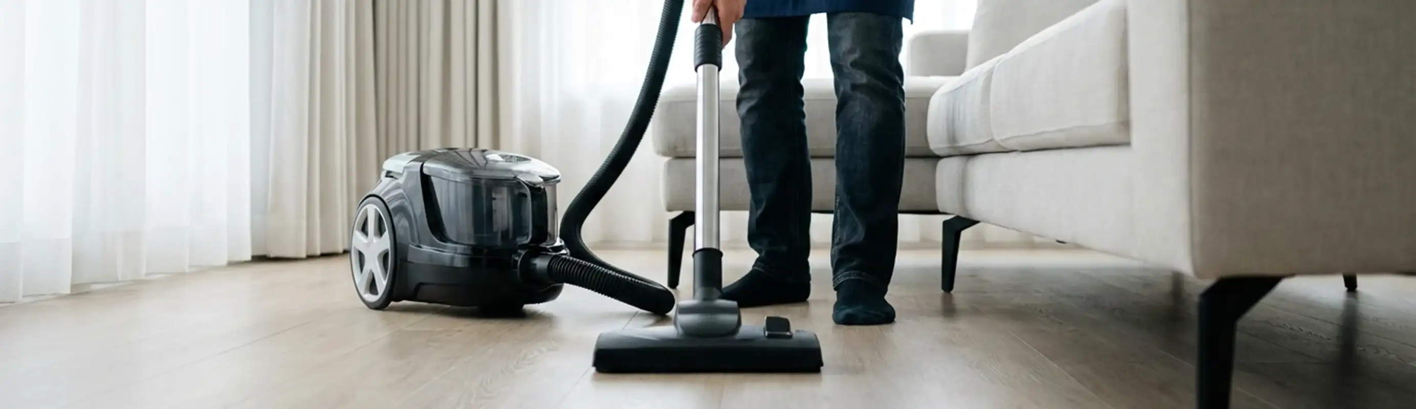 Professional house cleaner vacuuming a living room floor with a canister vacuum cleaner, Peoria, IL.
