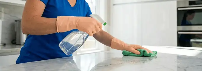 Maid service worker spraying and wiping a kitchen countertop with a microfiber cloth for sanitizing, Peoria, IL.
