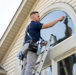 Professional window cleaner on a ladder using a squeegee to clean an exterior arched window, Peoria, IL.