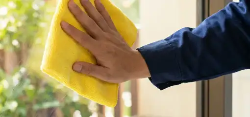 House cleaner wiping a glass window with a yellow microfiber cloth for streak-free cleaning, Peoria, IL.
